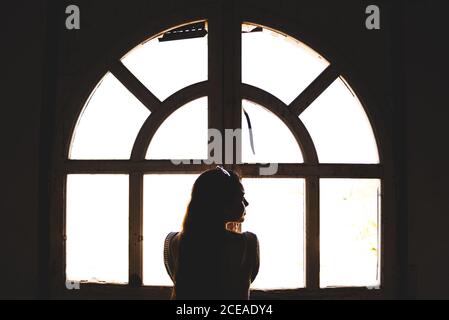 Silhouette einer jungen Frau, die in der Nähe eines schönen Fensters im alten Gebäude steht Stockfoto