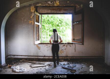 Silhouette einer jungen Frau, die in der Nähe eines schönen Fensters im alten Gebäude steht Stockfoto