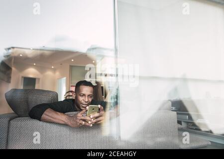 Erwachsene afroamerikanische Mann in Brille Buch lesen, während sitzen Auf dem Sofa zu Hause Stockfoto