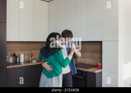 Junge Männer und Frauen in lässigen Outfits tanzen zusammen und haben Spaß in der stilvollen Küche zu Hause Stockfoto