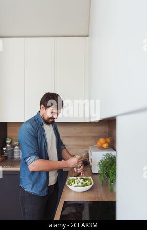 Seitenansicht des hübschen jungen Kerl lächelnd und gesund machen Salat im Stehen in der stilvollen Küche Stockfoto