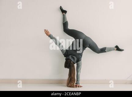 Rückansicht einer jungen sportlichen Frau, die im hellen Raum Handstand und Bein gespalten macht Stockfoto