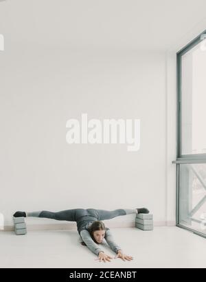 Junge, schlanke, sportliche Frau, die im Studio des hellen Zimmers ein Bein spaltet Stockfoto