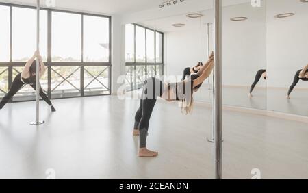 Zwei junge schlanke sportliche Frauen trainieren in der Nähe von Pole in Licht Zimmer Stockfoto
