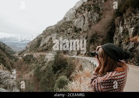 Seitenansicht der jungen Dame in Pullover und Hut die Foto Kamera zwischen den Hügeln in Pyrenäen Stockfoto