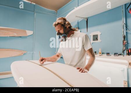 Mann in Atemschutzmaske Messung Surfbrett in der Werkstatt Stockfoto