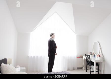 Seitenansicht des jungen, hübschen Mannes, der im weißen Schlafzimmer steht Und das Anziehen eines schwarzen formellen Kostüms Stockfoto