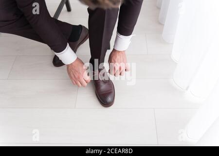 Junger Mann in schwarzem Kostüm und weißem Hemd sitzend Stuhl im Schlafzimmer und Lederschuhe anziehen Stockfoto