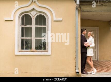 Seitenansicht der eleganten Braut und Bräutigam umarmen in der Nähe klein Altes Haus im grünen Garten Stockfoto