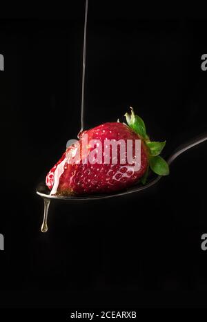 Nahaufnahme von frischen reifen roten Erdbeeren in fließendem Honigsirup auf schwarzem Hintergrund. Stockfoto