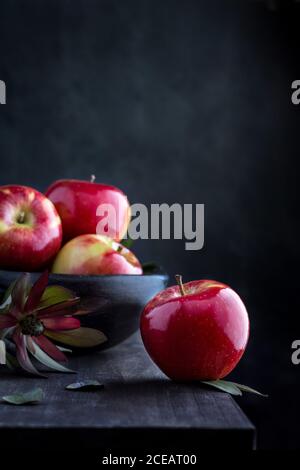 Frische rote Äpfel auf Holztisch und in einer Schüssel auf dunklem Hintergrund. Stockfoto