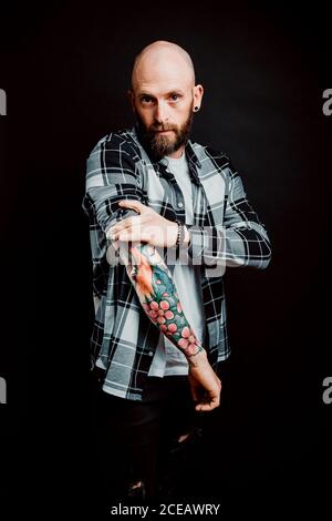 Bärtige haarlose Hipster in Shirt mit Tattoos auf Arme auf schwarzem Hintergrund Stockfoto