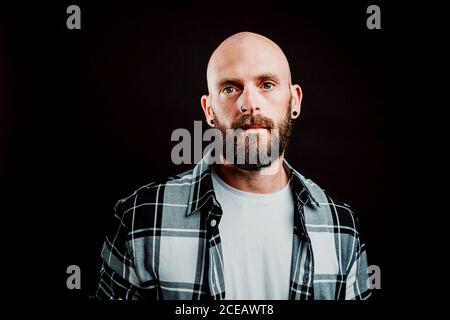 Bärtige haarlose Hipster in shirt Kamera schaut auf schwarzem Hintergrund Stockfoto