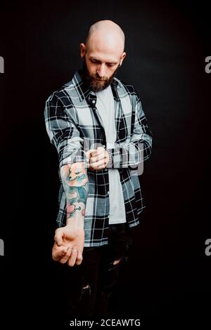 Bärtige haarlose Hipster in Shirt mit Tattoos auf Arme auf schwarzem Hintergrund Stockfoto