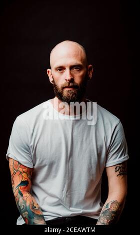 Unbehaarte Hipster in t Bärtigen-shirt mit Tattoos auf Arme auf schwarzem Hintergrund Stockfoto