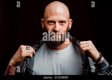 Bärtige haarlose Hipster in Shirt mit Tattoos auf Arme auf schwarzem Hintergrund Stockfoto