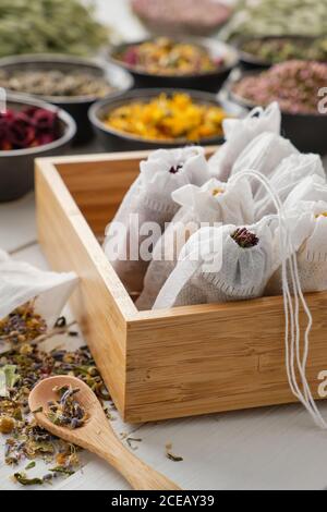 Holzkiste mit Filtertüten, gefüllt mit trockenen Heilkräutern und Blumen. Schwarze Schalen von Heilpflanzen auf dem Hintergrund. Alternative Medizin. Stockfoto