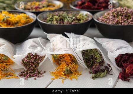 Filter Teebeutel gefüllt mit trockenen Heilkräutern - Majoran, Heidekraut, Ringelblumen und Rosenblüten. Schalen von Heilpflanzen auf dem Hintergrund. Altern Stockfoto