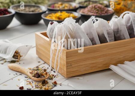 Holzkiste mit Teebeuteln gefüllt mit trockenen Heilkräutern und Blumen. Schalen von Heilpflanzen auf dem Hintergrund. Alternative Medizin Stockfoto