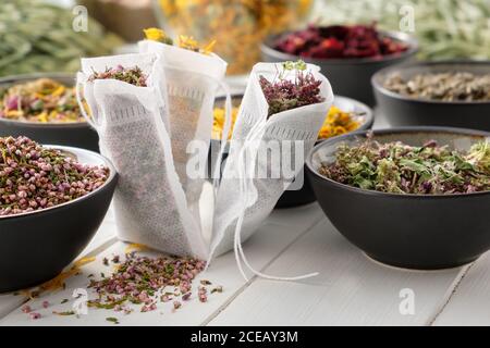 Filter Teebeutel gefüllt mit trockenen Heilkräutern - Majoran, Heidekraut, Ringelblumen und Rosenblüten. Schalen von Heilpflanzen auf Holztisch. Stockfoto