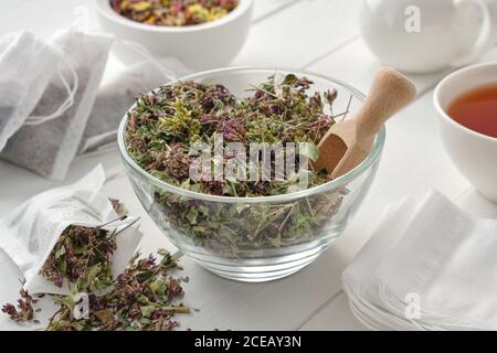 Schüssel mit trockenen Origanum vulgare Blumen, Teebeutel mit wilden Majoran Blumen gefüllt. Teetasse und Teekanne auf Holztisch. Alternative Medizin. Stockfoto