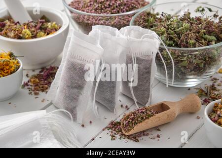 Filter Teebeutel mit gesunden Heilkräutern gefüllt. Schüsseln und Mörser aus trockenem Majoran, Heide und Ringelblumen auf Holztisch. Alternative medi Stockfoto