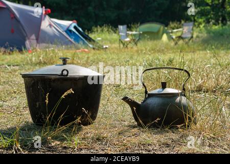 Touristenlager. Ein Wasserkocher und ein touristischer Kochtopf. Camping Zelte und Klappstühle auf dem Hintergrund. Stockfoto