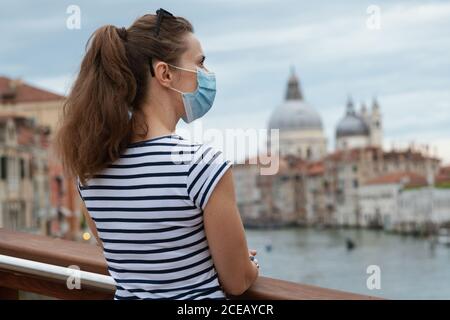 Reisen während einer Coronavirus-Pandemie. Von hinten gesehen moderne Solo-Tourist Frau mit medizinischer Maske genießen Promenade auf Accademia Brücke in Venedig, Ita Stockfoto