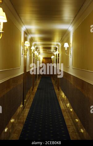 Schmaler Hotelkorridor mit Teppich und brennenden Wandlampen Und geschlossene Holztüren Stockfoto