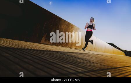 Junge Dame in Sportkleidung auf Wanderweg in sonniges Wetter mit blauem Himmel läuft Stockfoto