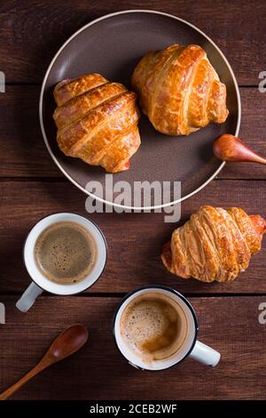 Von oben zwei Tassen Kaffee und Croissants auf Holztisch. Stockfoto