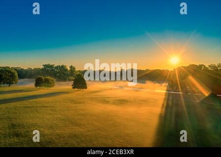 Wunderbarer nebliger Morgen im Münchens Englisher Garten, während der Sonnenaufgang andauert, goldene Lichtkulisse. Stockfoto