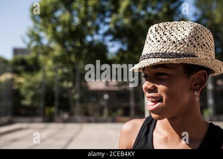 Afro Junge posiert mit Strohhut auf dem Basketball gericht seiner Nachbarschaft und lächelt Stockfoto