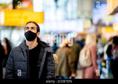 Ein Reisender, der eine Gesichtsmaske als vorbeugende Maßnahme am Flughafen sieht.Es ist wieder Geschäft am Flughafen Schiphol, da die Menschen während der Sommerferien jedoch mit obligatorischer Tragen von Gesichtsmasken reisen. Die Fluggesellschaft KLM erhielt aufgrund der Auswirkungen der Coronavirus-Krise auf den Flughafen ein Hilfspaket in Höhe von 3.4 Milliarden Euro. Stockfoto