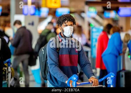 Ein Reisender, der eine Gesichtsmaske als vorbeugende Maßnahme am Flughafen sieht.Es ist wieder Geschäft am Flughafen Schiphol, da die Menschen während der Sommerferien jedoch mit obligatorischer Tragen von Gesichtsmasken reisen. Die Fluggesellschaft KLM erhielt aufgrund der Auswirkungen der Coronavirus-Krise auf den Flughafen ein Hilfspaket in Höhe von 3.4 Milliarden Euro. Stockfoto