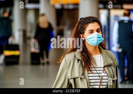 Ein Reisender, der eine Gesichtsmaske als vorbeugende Maßnahme am Flughafen sieht.Es ist wieder Geschäft am Flughafen Schiphol, da die Menschen während der Sommerferien jedoch mit obligatorischer Tragen von Gesichtsmasken reisen. Die Fluggesellschaft KLM erhielt aufgrund der Auswirkungen der Coronavirus-Krise auf den Flughafen ein Hilfspaket in Höhe von 3.4 Milliarden Euro. Stockfoto