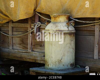 Alte rostige Milchkanne, die vor einem Planwagen sitzt. Stockfoto