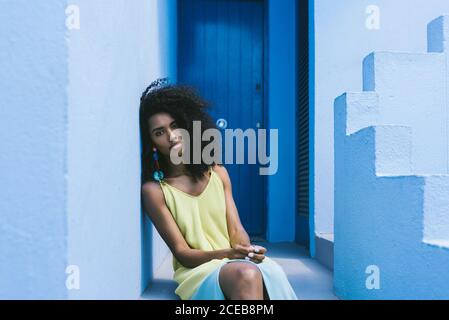 Schwarze Frau, die in einer blauen Gebäudetreppe sitzt.