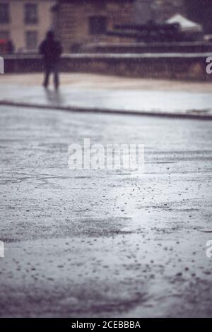 Nahaufnahme der Regentropfen auf der Straße von Paris während Regen auf dem Hintergrund der Wanderperson in schwarzer Kleidung Stockfoto