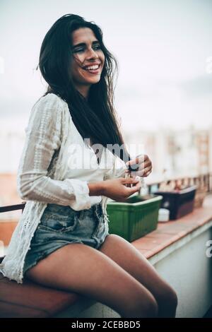 Junge Frau, die auf dem Balkon sitzt und lächelt Stockfoto