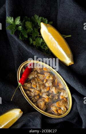 Blechdose mit köstlichen Meeresfrüchten serviert mit Pfeffer und Zitrone auf schwarzem Stoff Hintergrund. Stockfoto