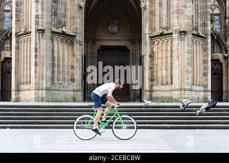 Seitenansicht des jungen Mannes auf dem grünen Fahrrad vorbei historischen Gebäude in der Stadt Stockfoto