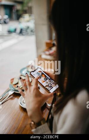 Anonyme Frau, die während der Aufnahme von frischem Kaffee und Snacks Sitzen am Tisch im Café Stockfoto