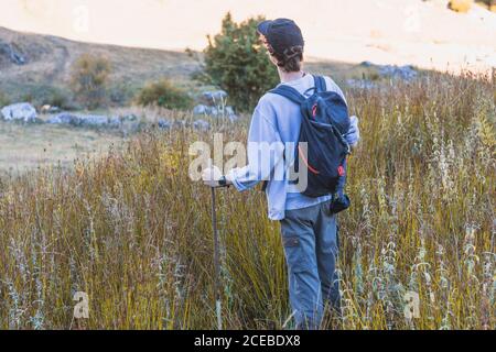 Von oben Rückansicht des Mannes mit Rucksack und Trekking Stöcke stehen auf einem Hügel und schauen sich um Stockfoto