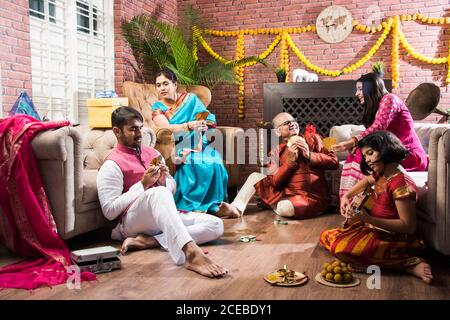 Happy Indian Family spielt teen patti oder drei Karten Spiel Auf diwali Festival Nacht in traditioneller Kleidung zu Hause Stockfoto