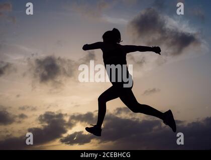Von unten Silhouette der jungen Dame, die in Sportbekleidung und wunderbaren Himmel mit Wolken in Abend Stockfoto