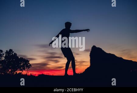 Silhouette einer nicht erkennbaren Person, die in den Abendlichtern am Felsen steht. Stockfoto