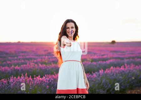 Lächelnde junge Frau, die Blume zwischen violettem Lavendelfeld zeigt Stockfoto