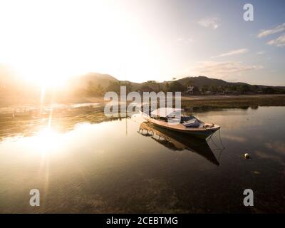 Kleines Motorboot mit Rasen und Strasse an der Küste festgemacht Sonniger Sommertag Stockfoto