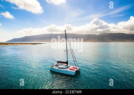 Luftaufnahme einer kleinen Yacht, die an sonnigen Sommertagen in La Graciosa, Kanarische Inseln, in einer malerischen Bucht an der felsigen Meeresküste navigiert Stockfoto